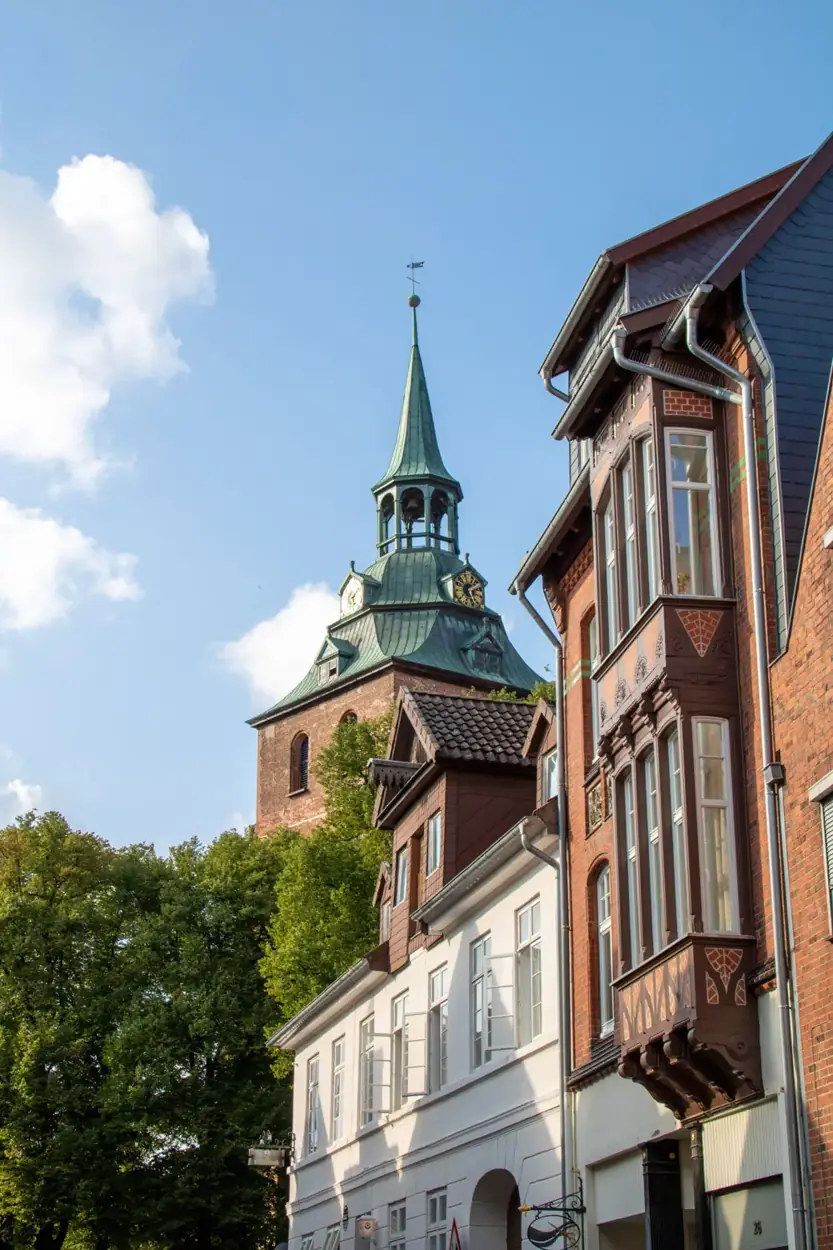 Kirchturm mit grüner Haube hinter Häusern mit Erkern