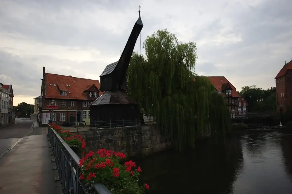 Alter Kran an der Ilmenau an einem Augustmorgen, Trauerweide, Geranien am Geländer, dunkles Wasser